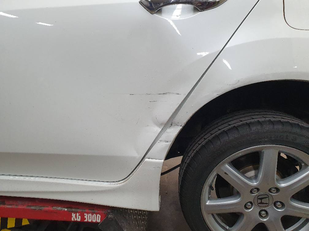 Ein weißes Auto mit einem beschädigten Kotflügel steht auf einer Hebebühne.