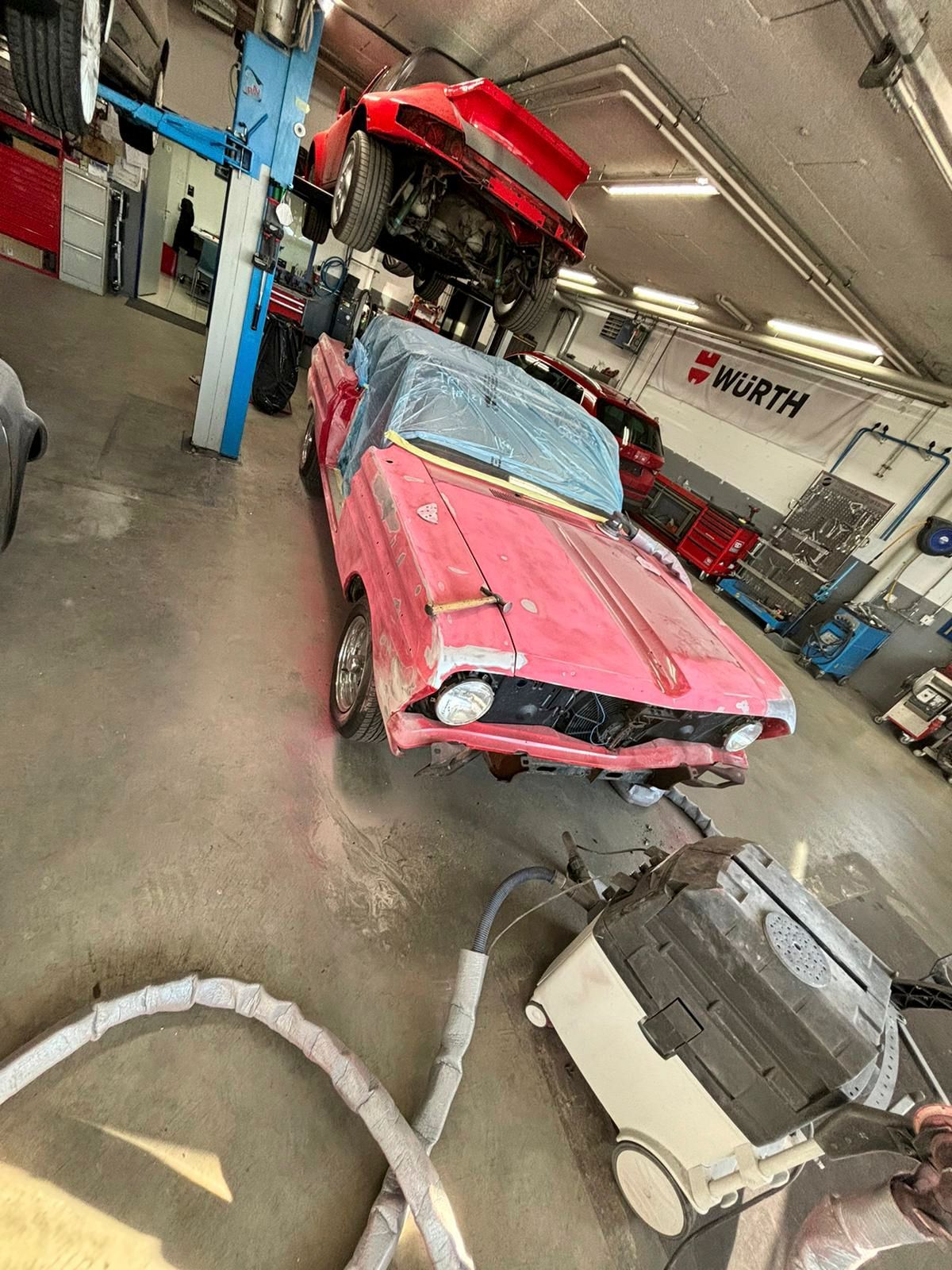 In einer Garage steht ein rosa Auto auf einem anderen Auto.