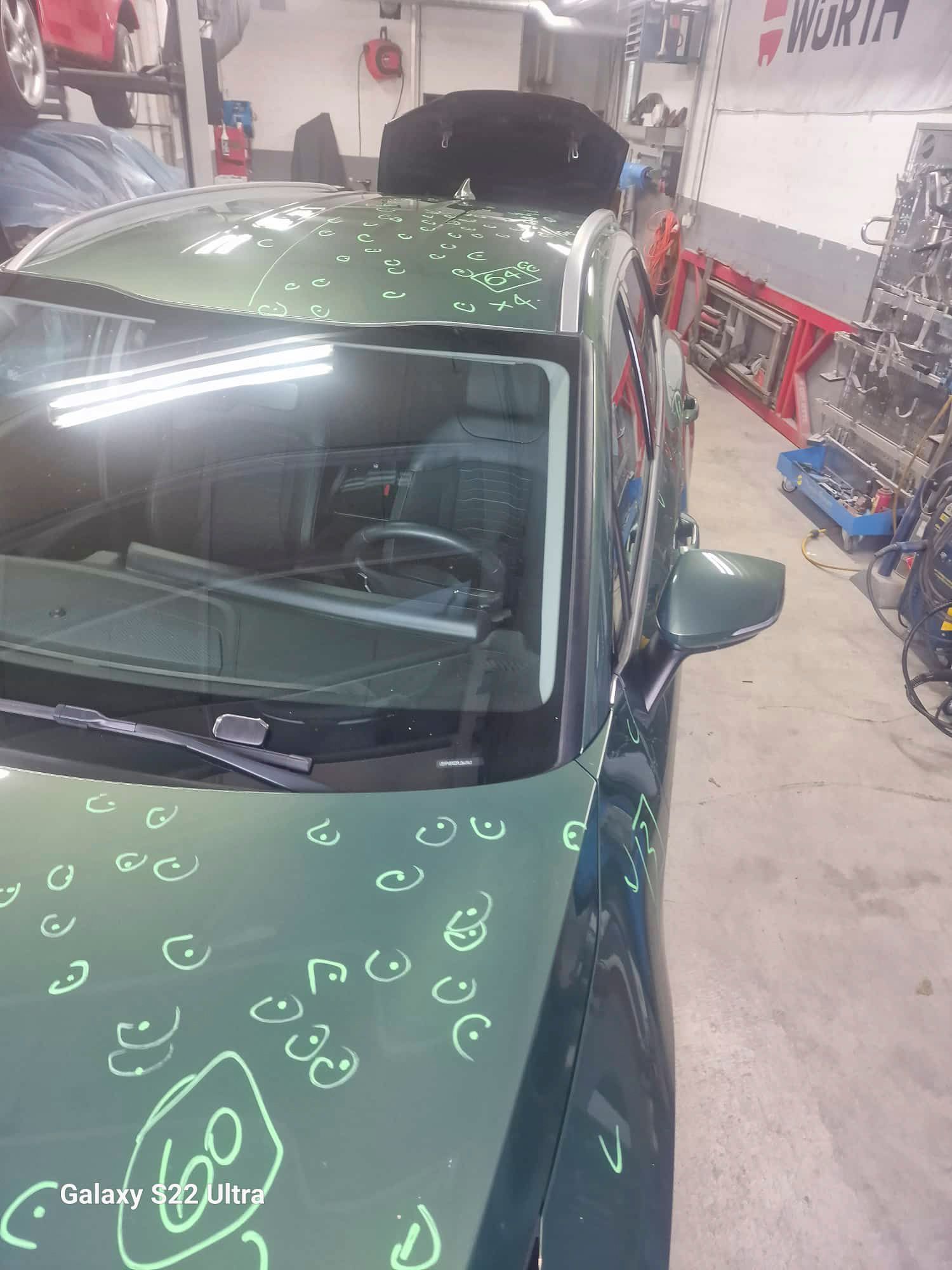 Ein grünes Auto mit Hagelschäden auf dem Dach steht in einer Garage.