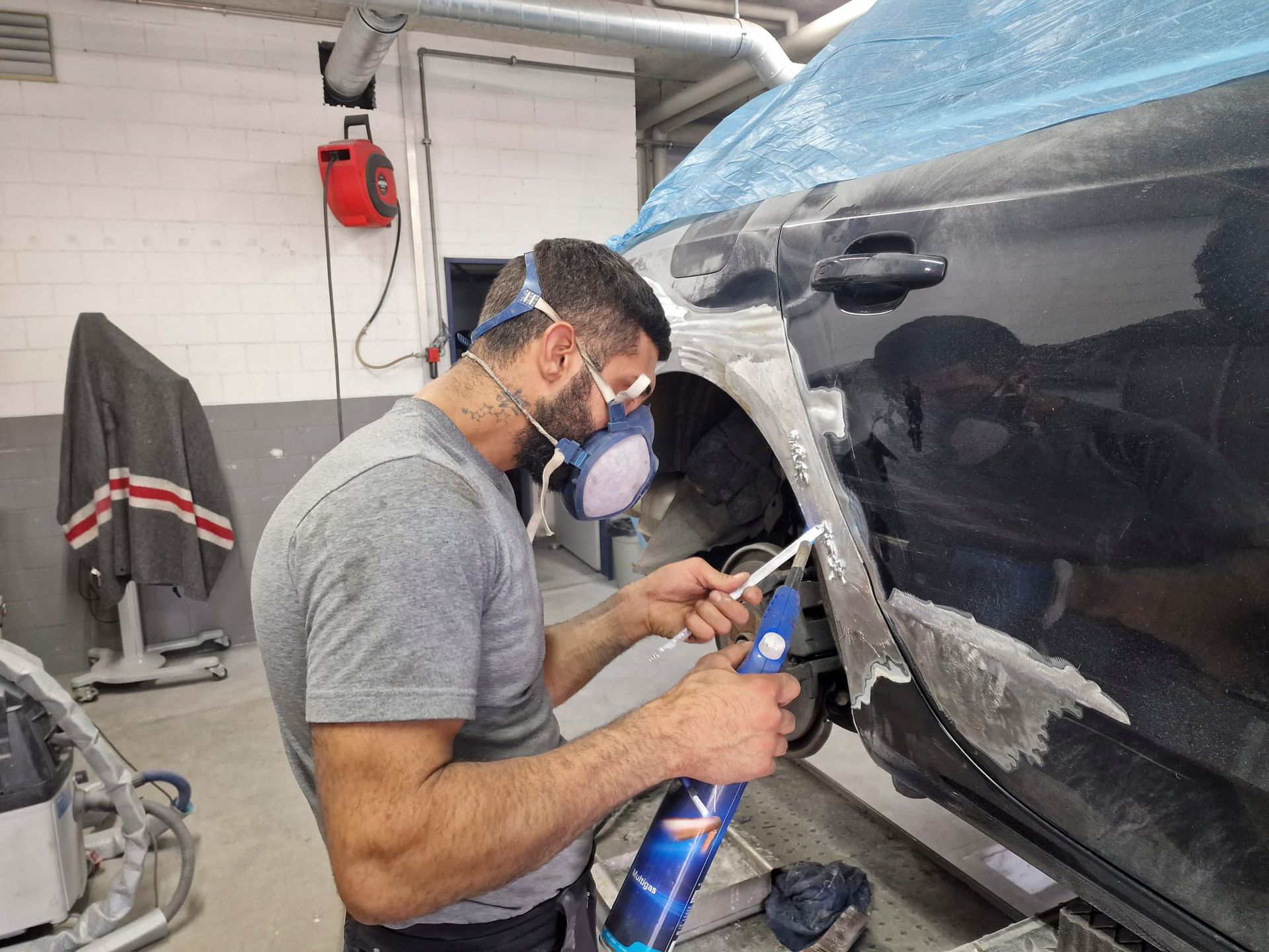 Ein Mann mit einer Maske arbeitet in einer Garage an einem Auto.