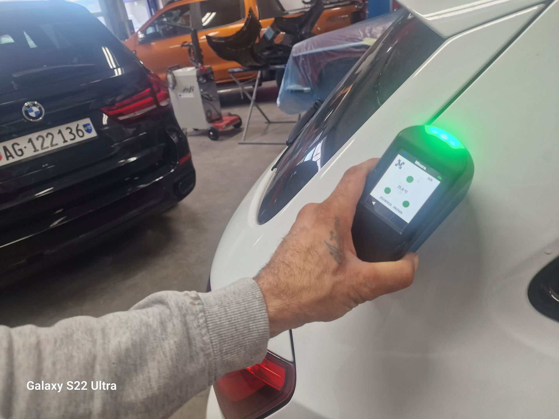 Eine Person hält ein Gerät vor einem weißen Auto.