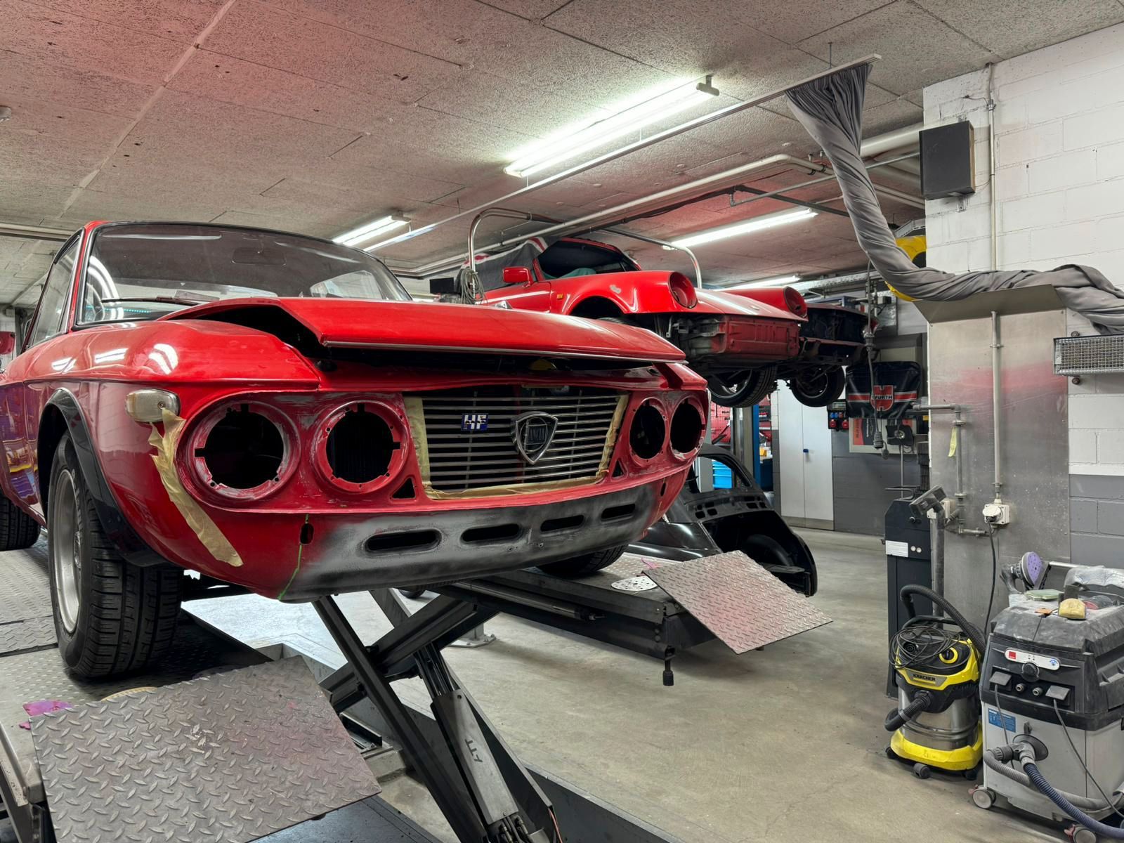 Ein rotes Auto steht auf einer Hebebühne in einer Garage.