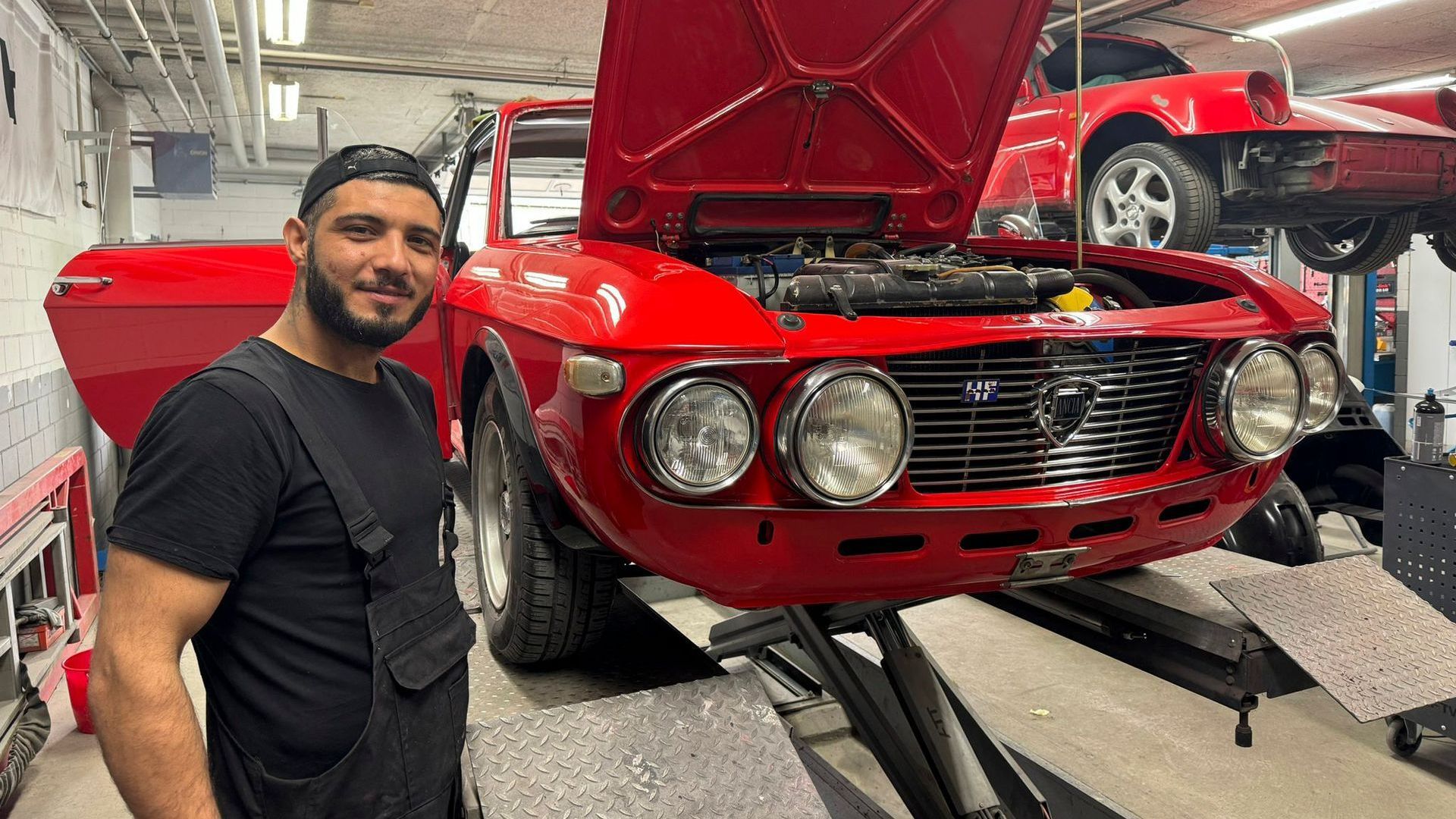 Ein Mann steht vor einem roten Auto in einer Garage.