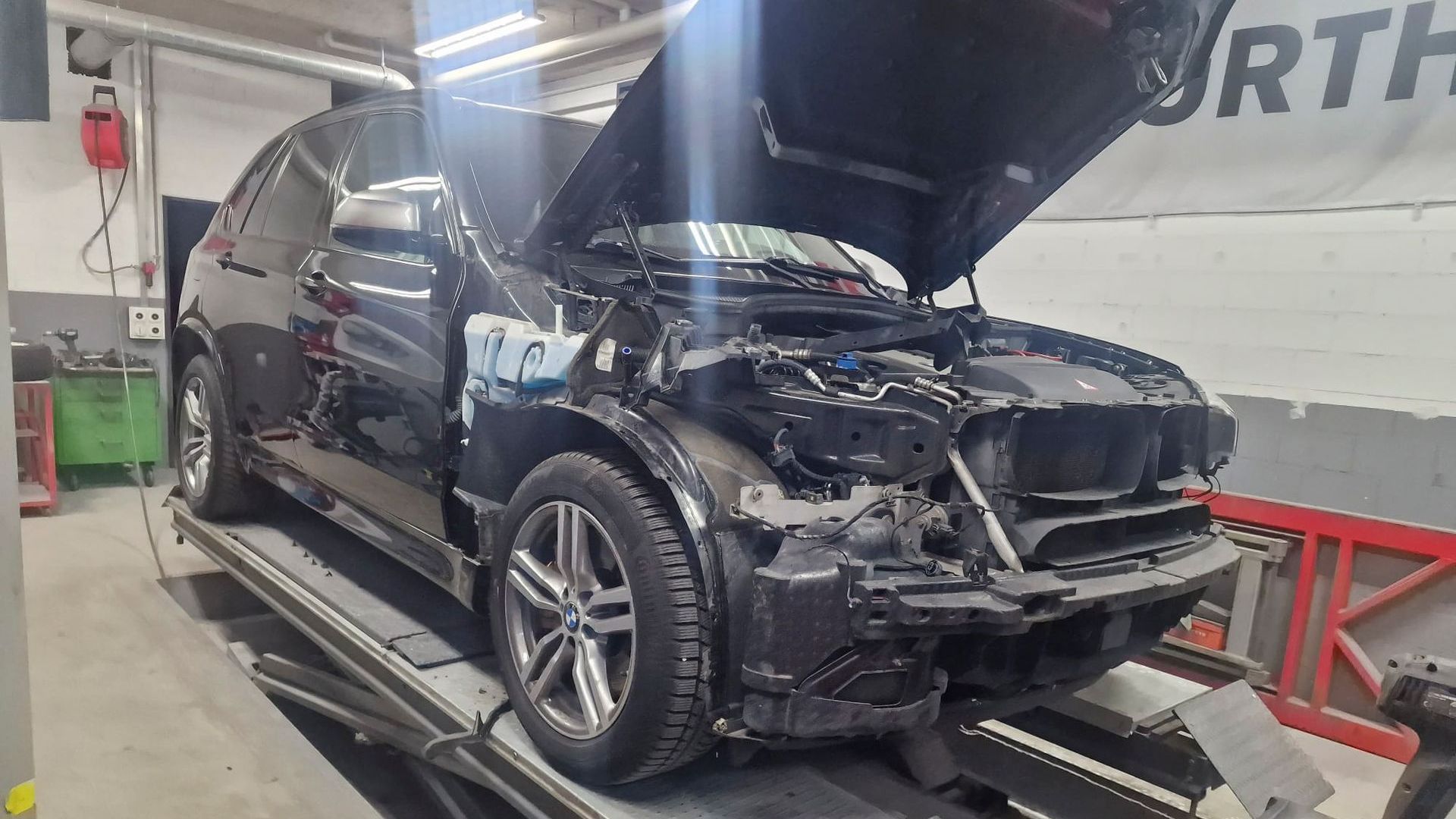 Ein Auto mit geöffneter Motorhaube steht auf einer Hebebühne in einer Garage.