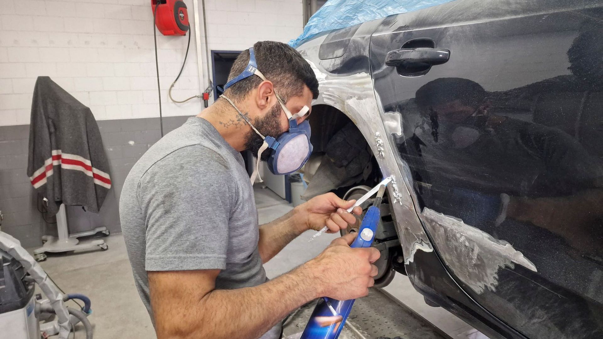 Ein Mann mit einer Maske arbeitet in einer Garage an einem Auto.