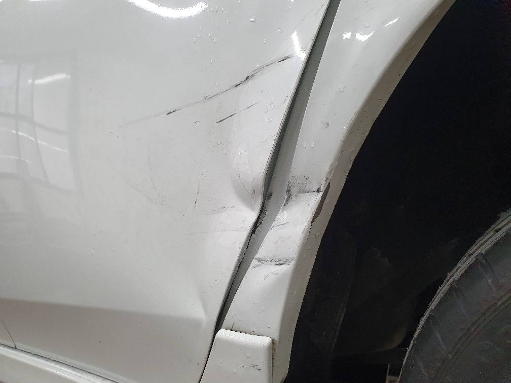 Eine Nahaufnahme eines weißen Autos mit einem beschädigten Kotflügel.