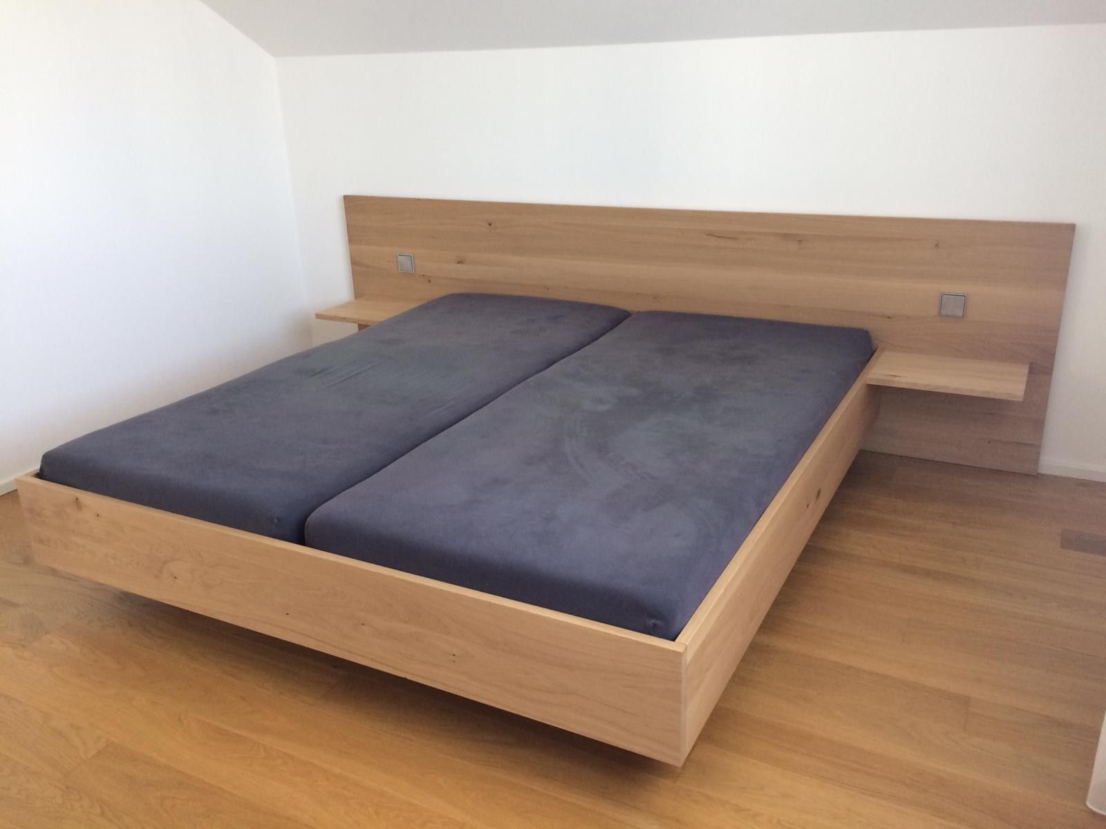 Holzbett mit zwei Matratzen, Kopfteil und angebrachten Nachttischen in einem Schlafzimmer.