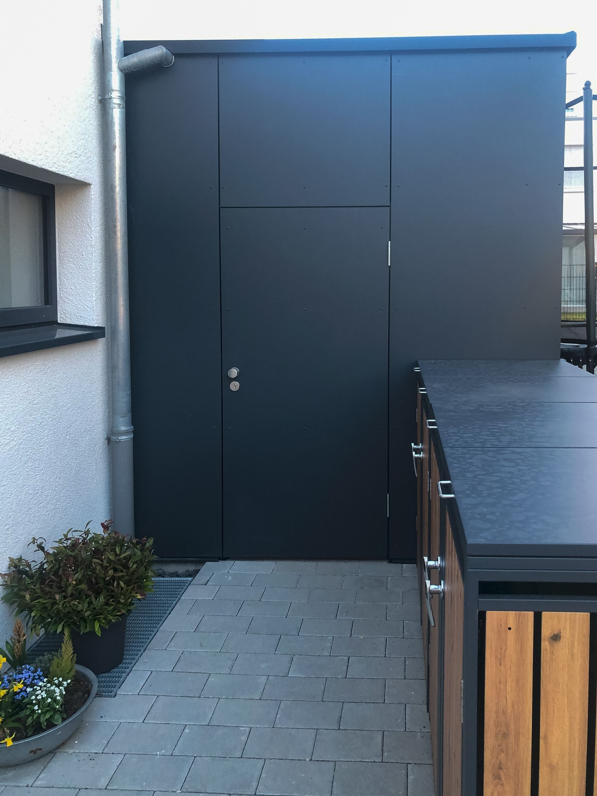 Neben einem gemauerten Gehweg befindet sich eine schwarze Tür.