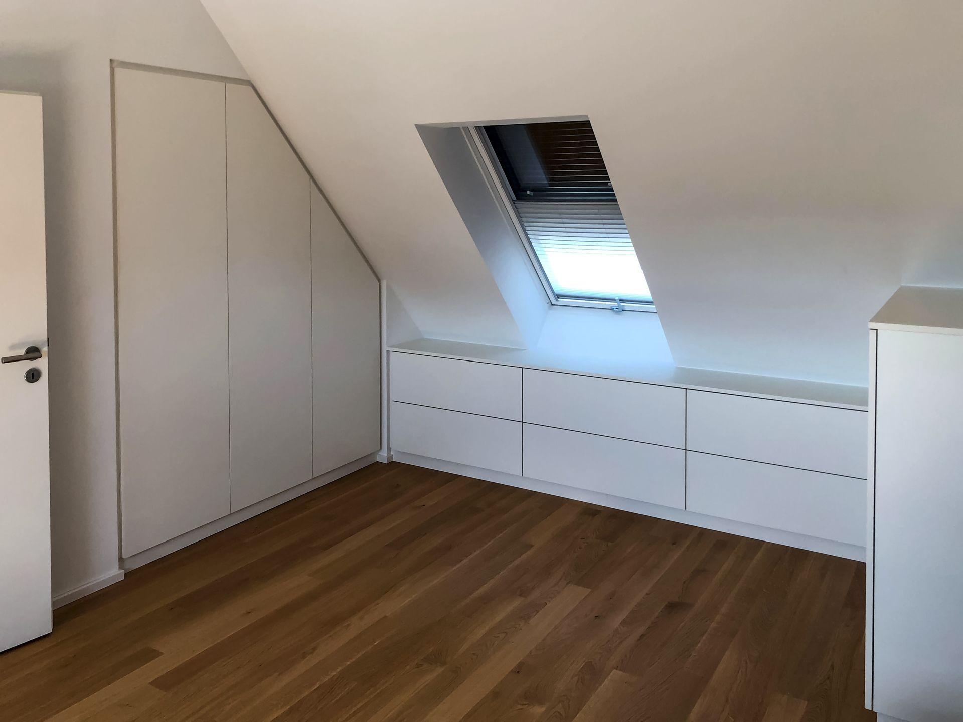 Ein Raum mit schräger Decke und einem Fenster