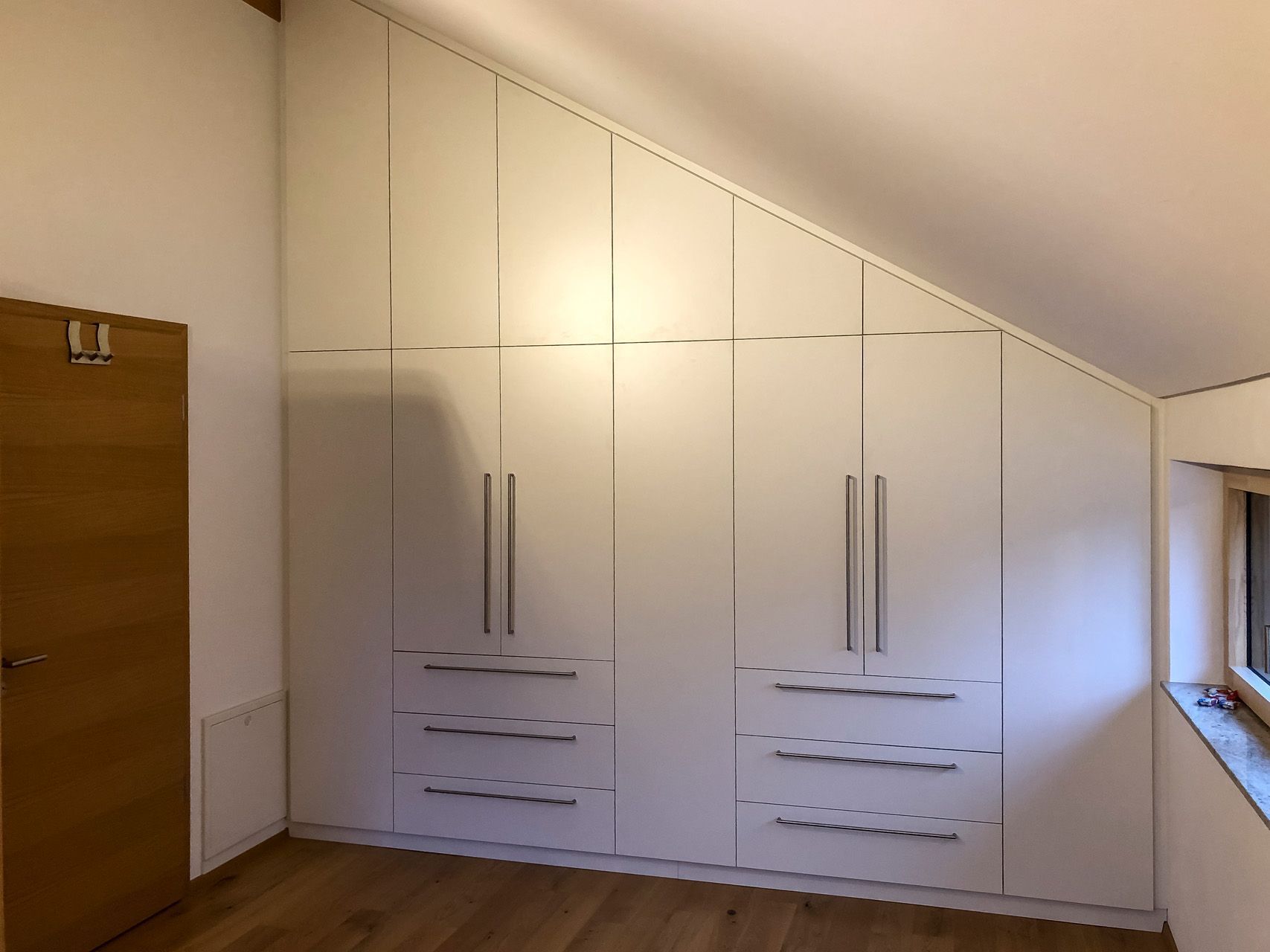 Ein Schlafzimmer mit Dachschräge und weißen Schränken und Schubladen.