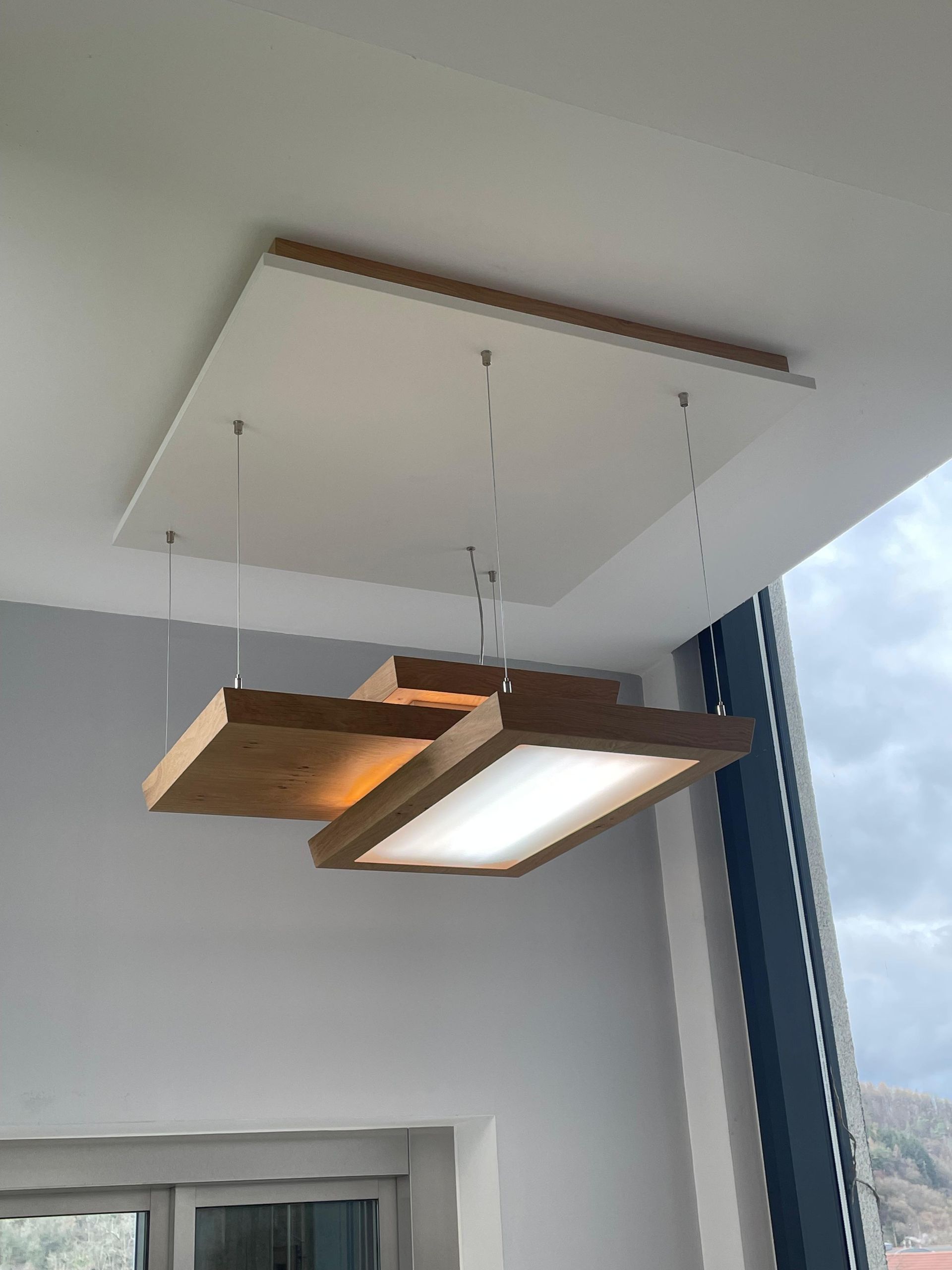 Vor einem Fenster hängt eine hölzerne Lampe von der Decke.