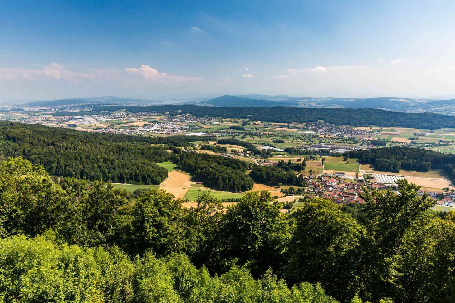 Malerische Ansicht einer Stadt in einem Tal, umgeben von grünen Bäumen, Feldern und einem klaren blauen Himmel.