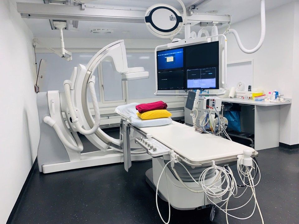 Angiographieraum mit medizinischer Ausrüstung, Untersuchungstisch und Monitoren.