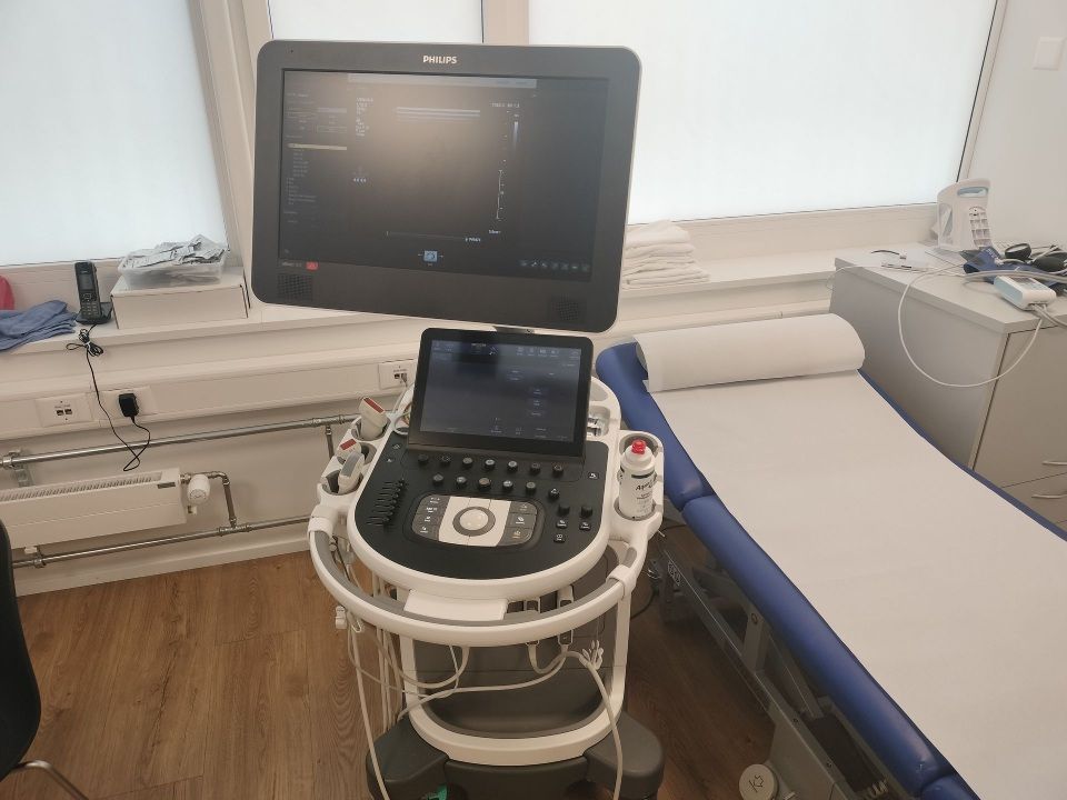 Ultraschallgerät im Untersuchungsraum. Rechts davon steht ein Bett.