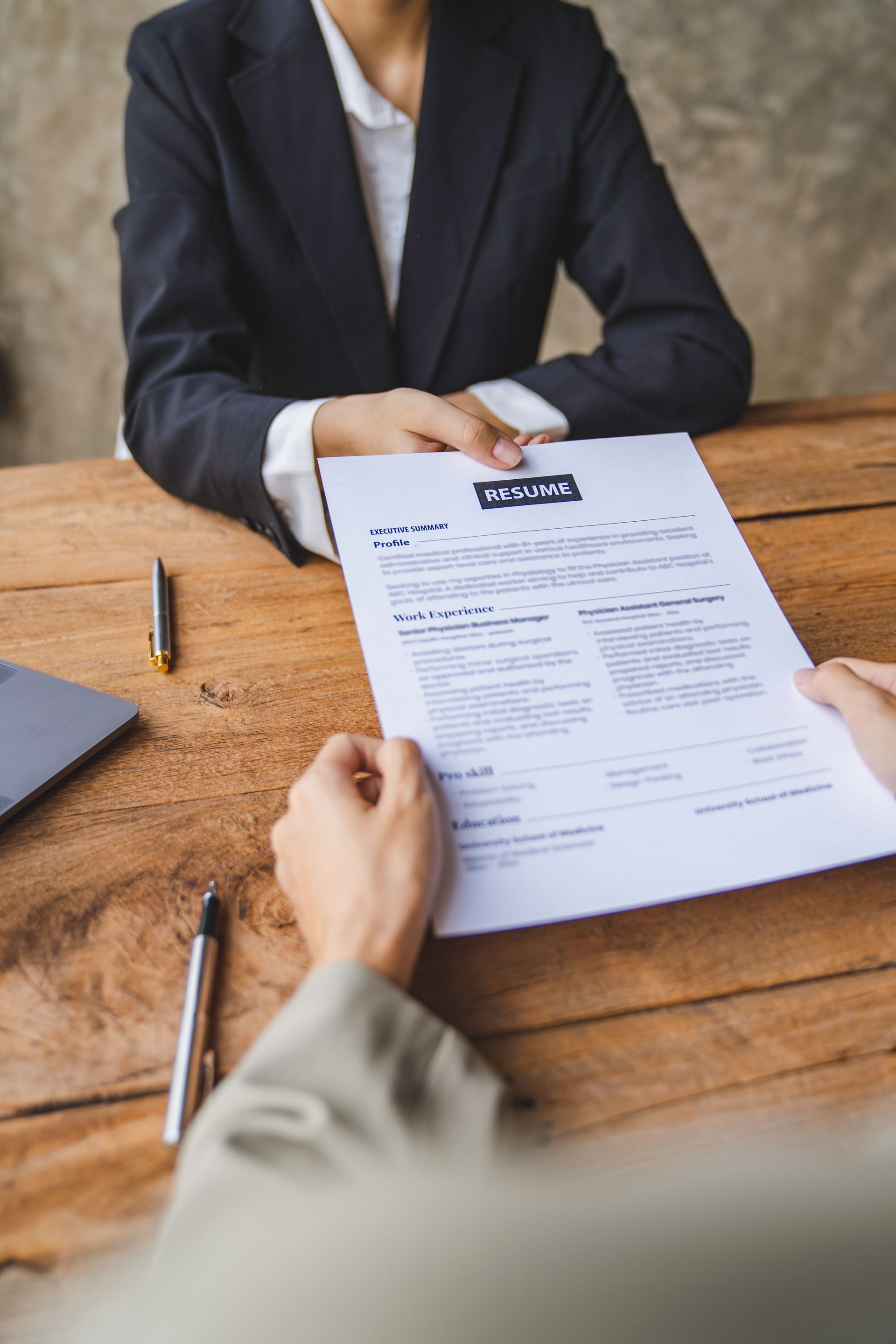 Des mains se passent un CV au-dessus d'une table en bois.