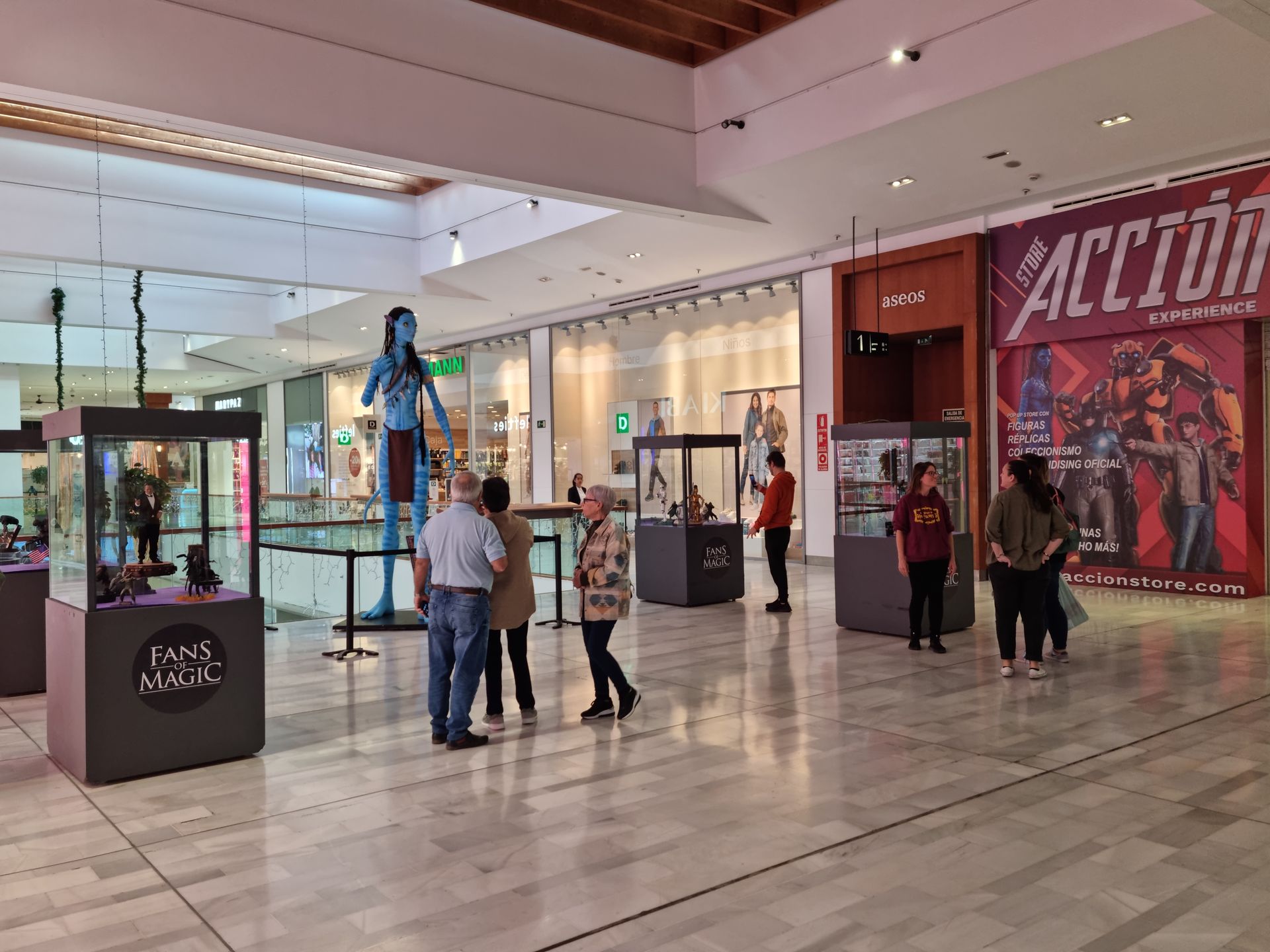 Un grupo de personas está de pie en un centro comercial mirando una exhibición de figuras de acción.