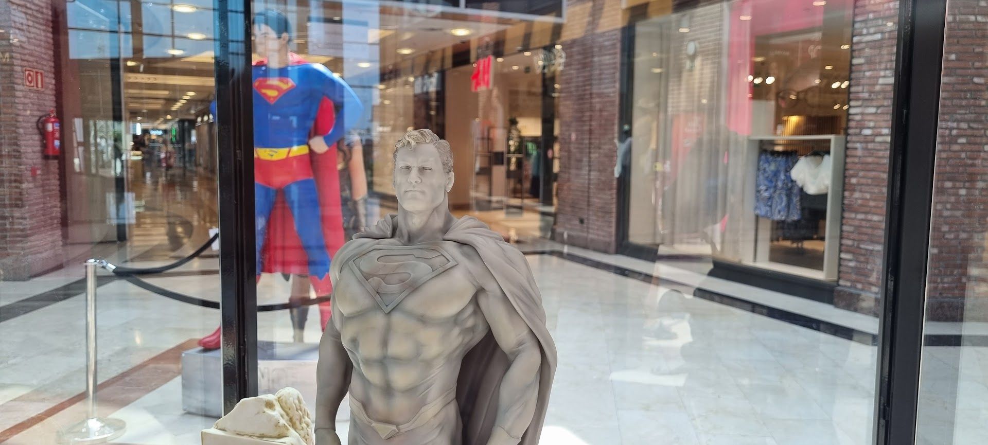 Una estatua de Superman está parada frente al escaparate de una tienda.