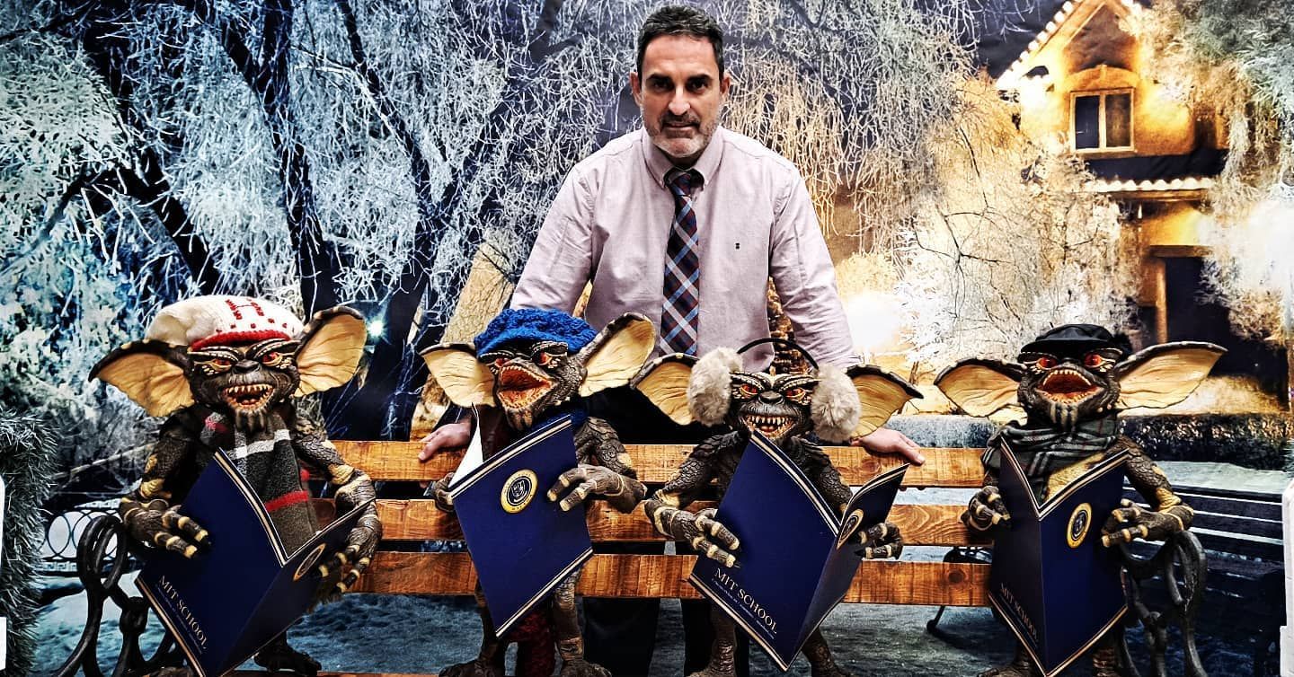 Un hombre con corbata está de pie junto a tres gremlins en un banco.