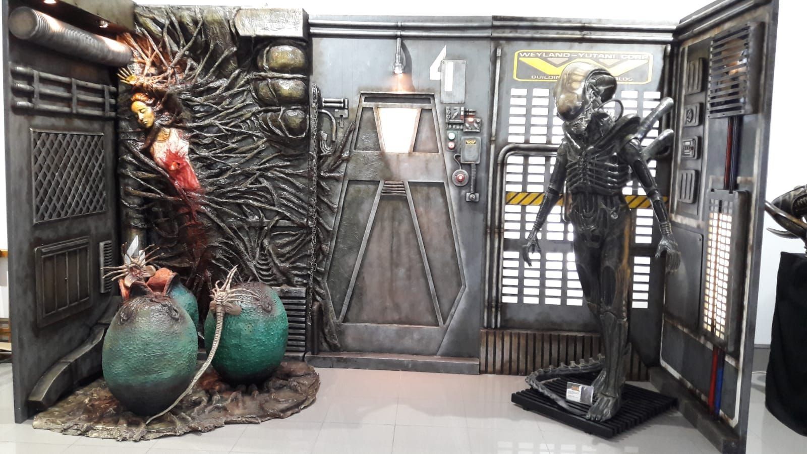 Una estatua de un hombre de pie junto a dos huevos extraterrestres en una habitación.