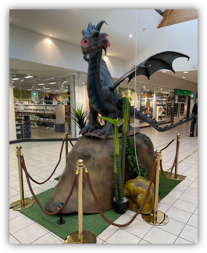 Una estatua de un dragón sentado en lo alto de una roca en un centro comercial.