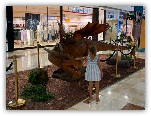 Una niña se encuentra frente a una estatua de un dragón en un centro comercial.