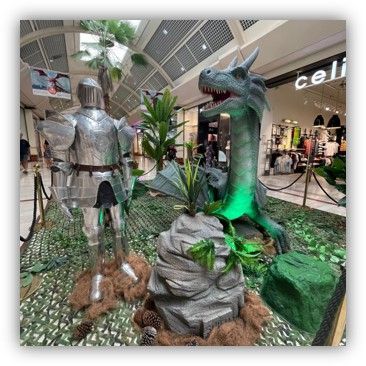 Un caballero con armadura está de pie junto a un dragón en un centro comercial.