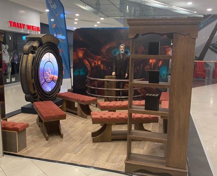 Un hombre con traje está parado frente a un expositor en un centro comercial.