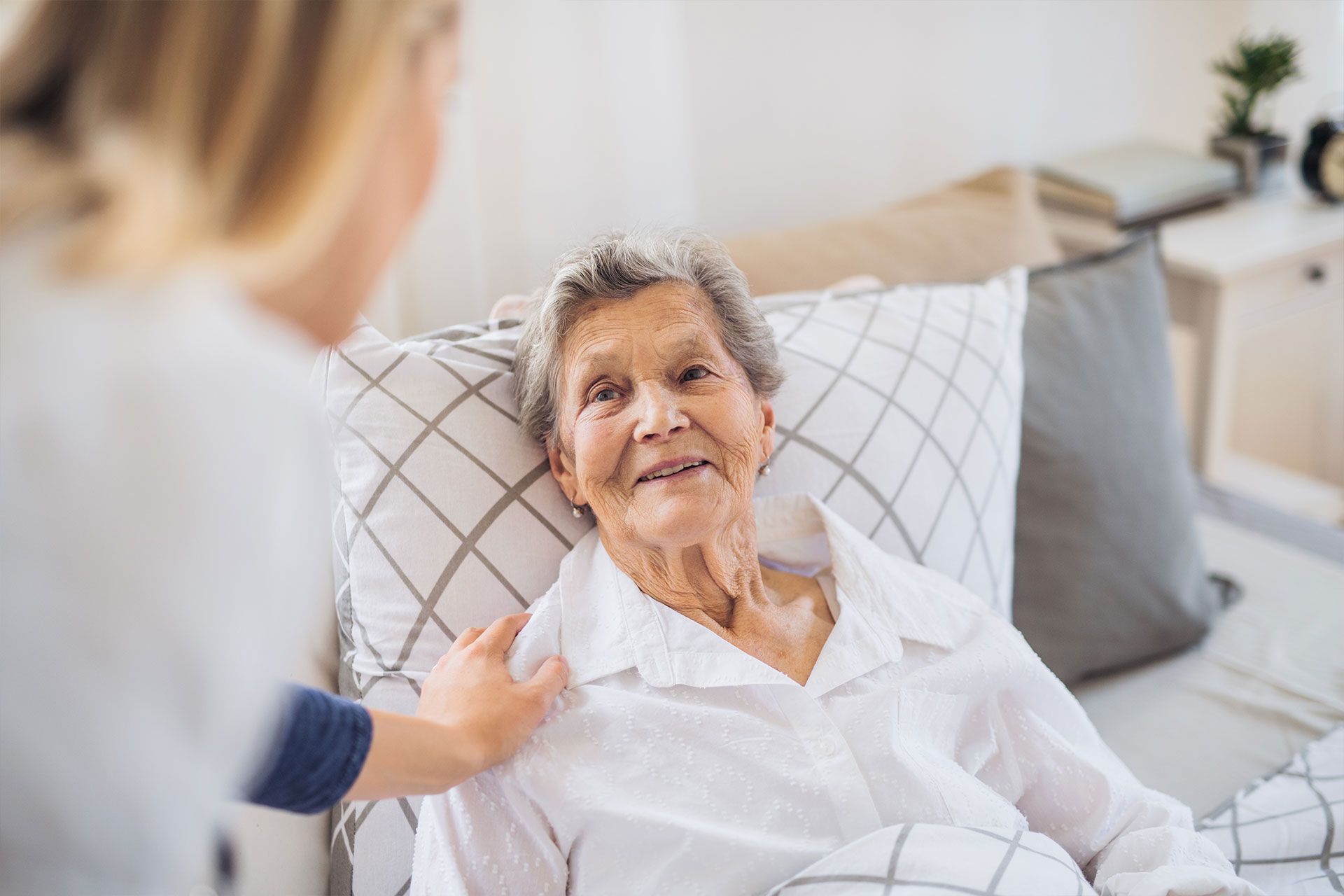 Eine ältere Frau liegt in einem Krankenhausbett und spricht mit einer Krankenschwester.