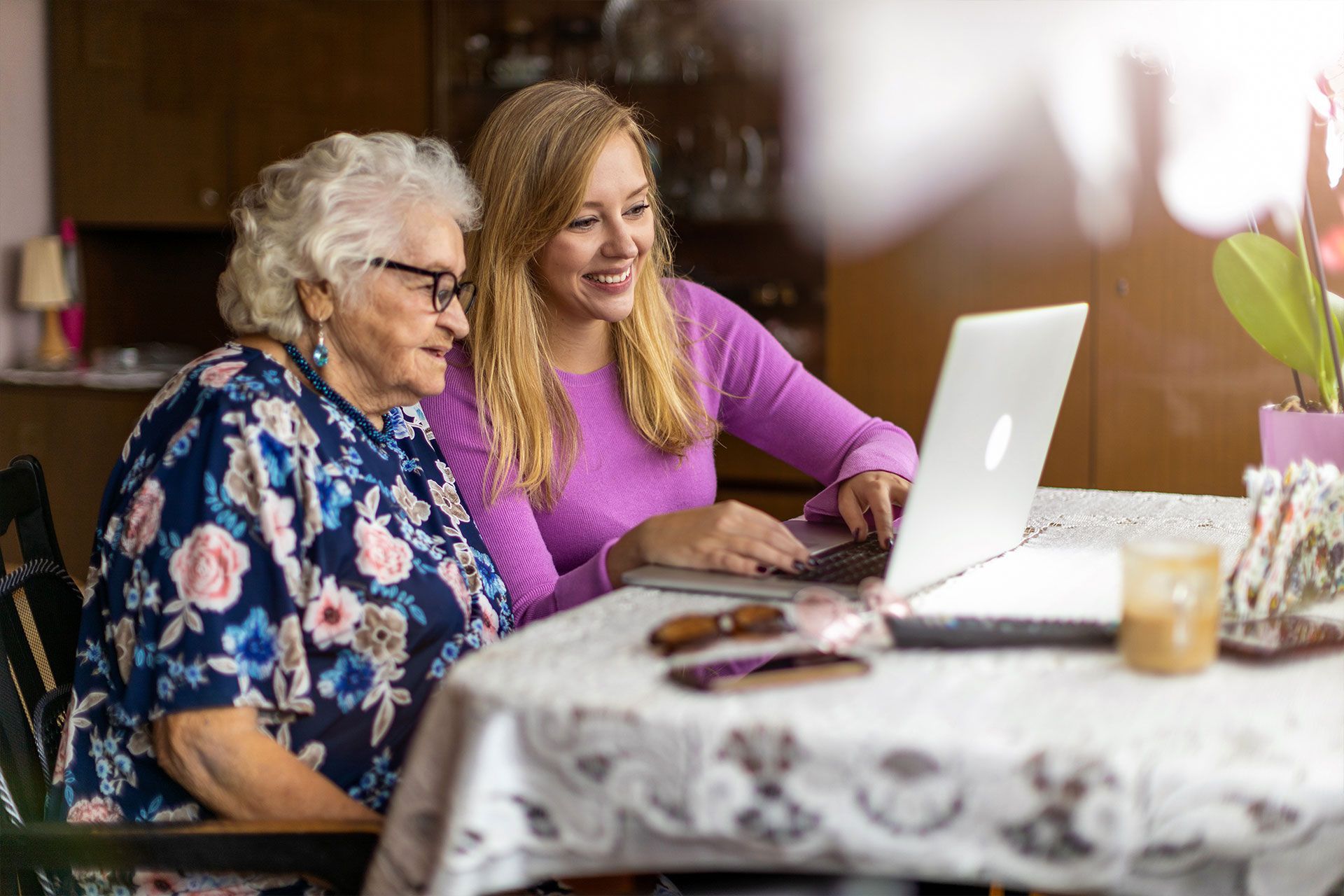 Eine junge Frau hilft einer älteren Frau bei der Benutzung eines Laptops.