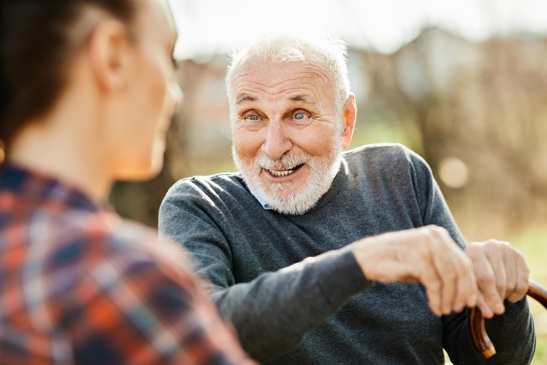 Ein älterer Mann mit einem Stock spricht mit einer jungen Frau.