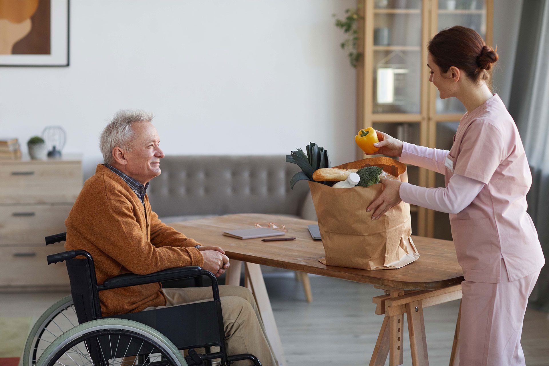Eine Krankenschwester gibt einem älteren Mann im Rollstuhl eine Tüte mit Lebensmitteln.