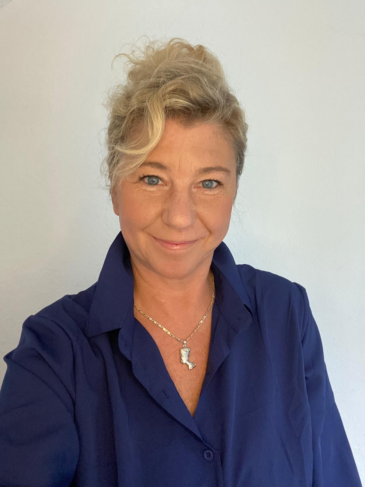 Eine Frau mit einem blauen Hemd und einer Halskette lächelt in die Kamera.