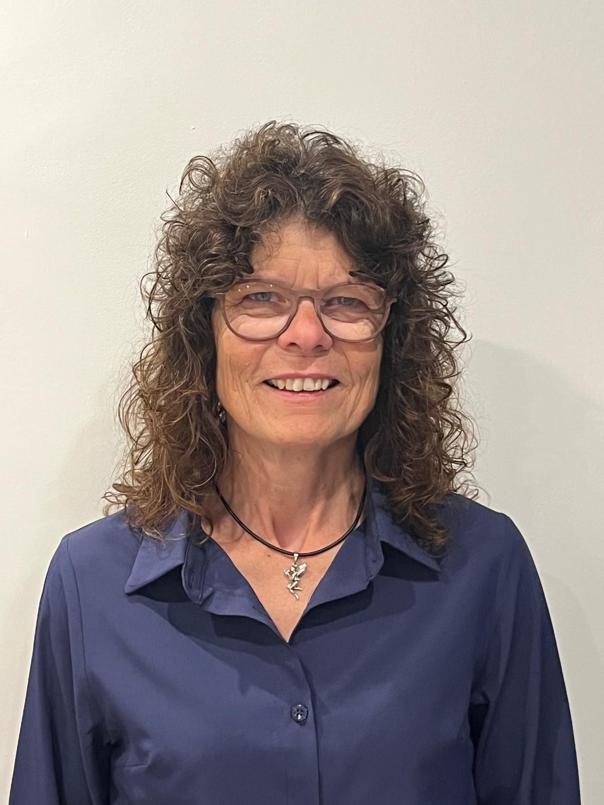 Eine Frau mit Brille und blauem Hemd lächelt in die Kamera.