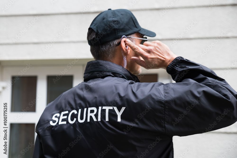 Sicherheitsbeamter in schwarzer Jacke und Mütze salutiert vor einem Gebäude