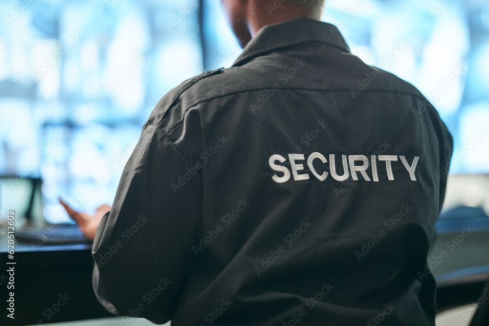 Sicherheitsmann in schwarzer Jacke mit der Aufschrift „SECURITY“ auf dem Rücken, steht drinnen in der Nähe eines hellen Fensters.