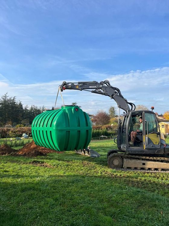 Une excavatrice soulève un grand réservoir sphérique vert sur un champ herbeux sous un ciel bleu