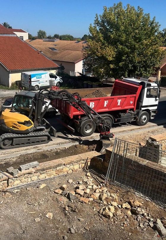 Minipelle et camion-benne rouge sur un chantier de construction résidentielle avec des gravats et des murs de soutènement