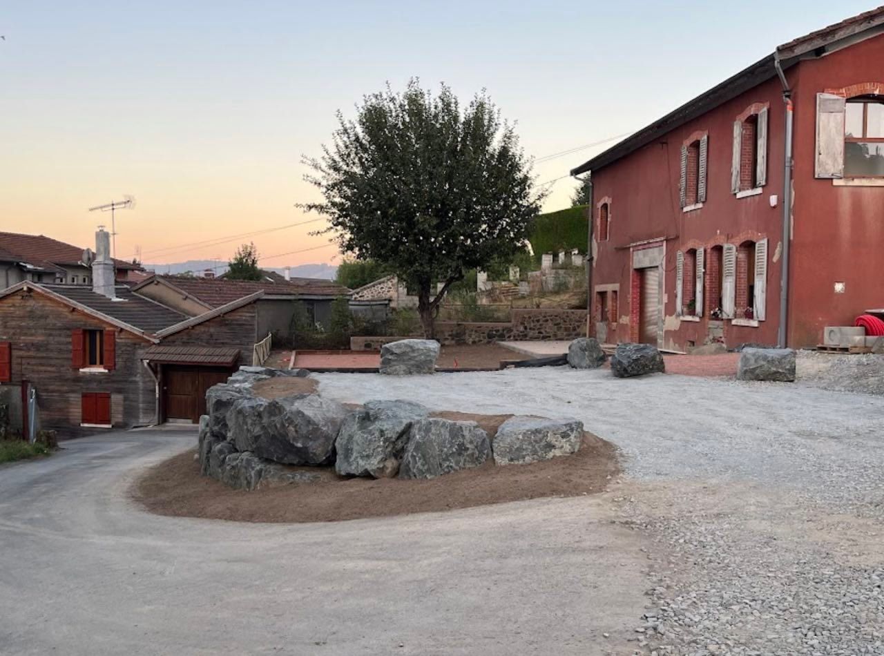 Cour rurale avec des bâtiments rouges, un arbre et de gros rochers au coucher du soleil