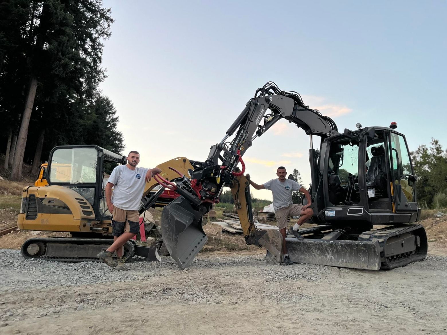 Deux hommes posent avec des excavatrices sur un site de gravier au crépuscule