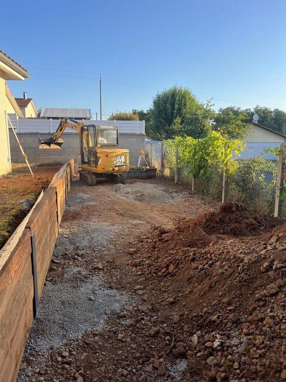 Chantier de construction avec une excavatrice creusant une tranchée de terre à côté d'une maison au coucher du soleil