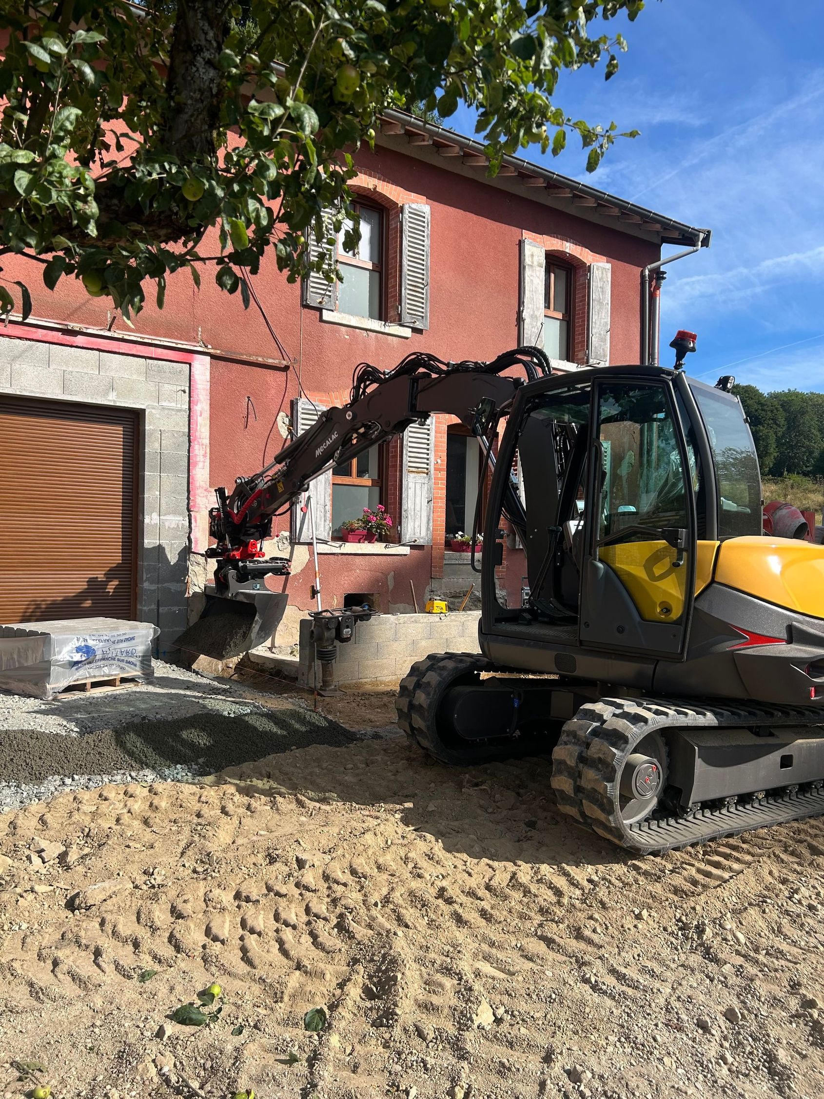 Une pelleteuse jaune creuse au bord d'un étang boueux, sous les arbres