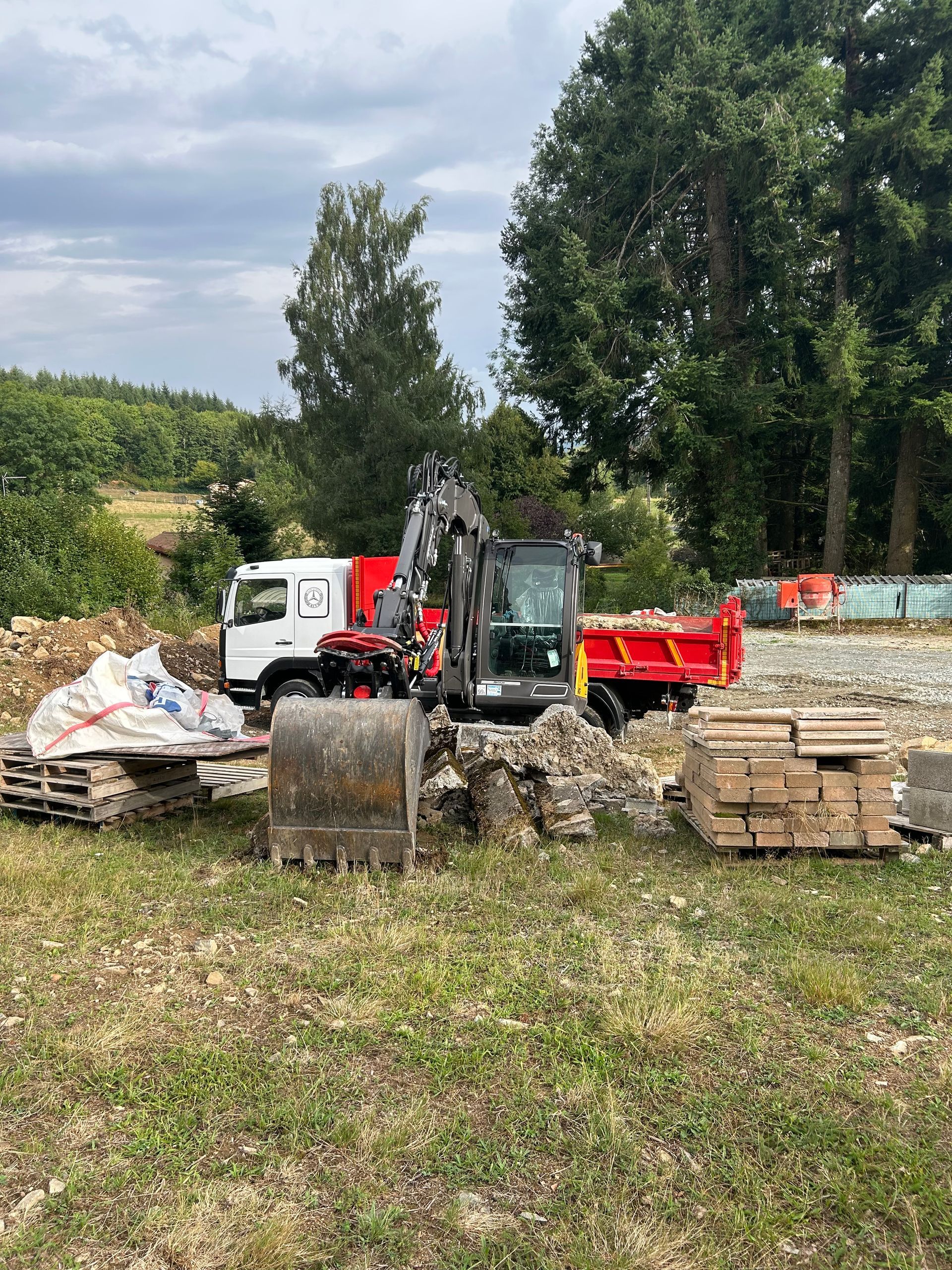 Cour de campagne avec une excavation de terre à côté d'une maison rouge et un monticule herbeux sous un ciel nuageux