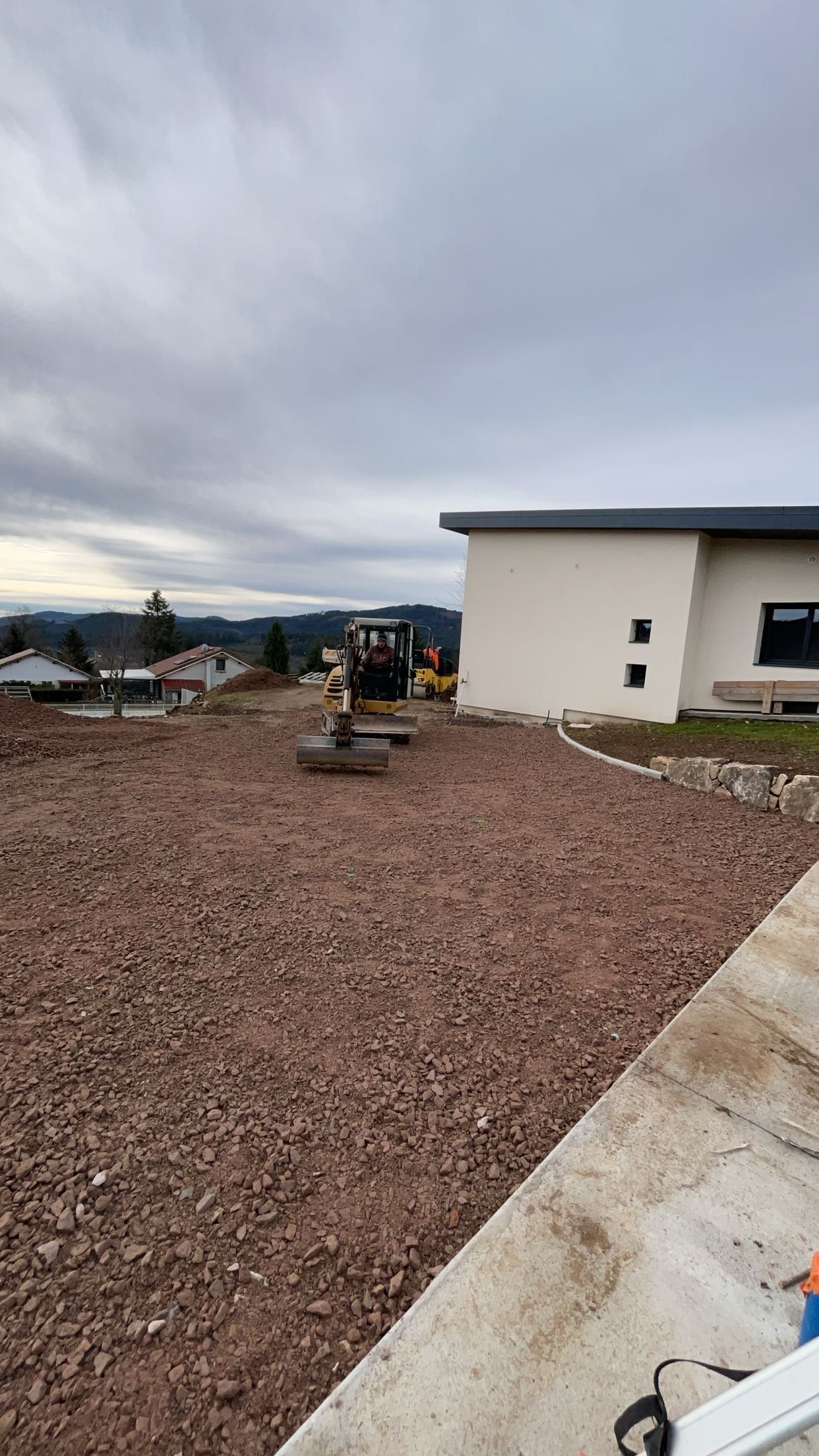 Une pelleteuse creuse un grand trou dans un jardin à côté d'une maison, la terre étant entassée autour.
