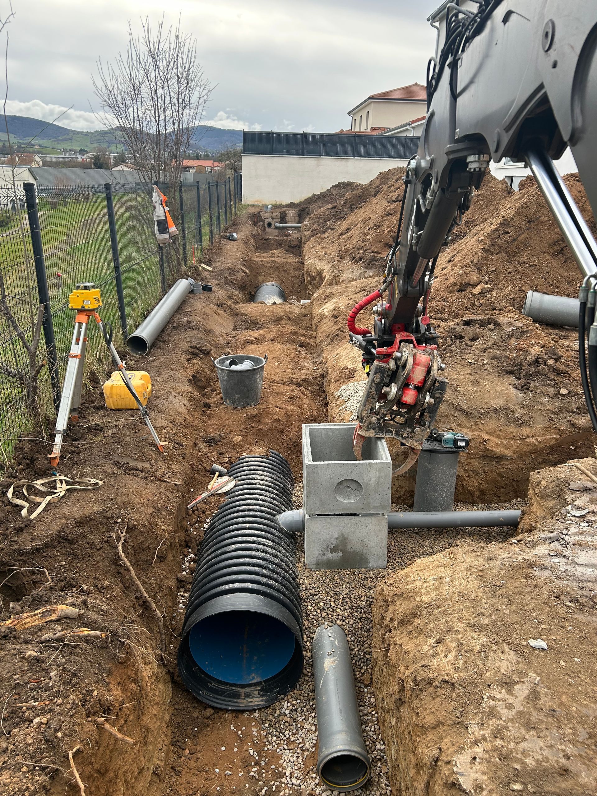 Tranchée de construction avec tuyau noir installé à côté d'une excavatrice et des fondations de la maison