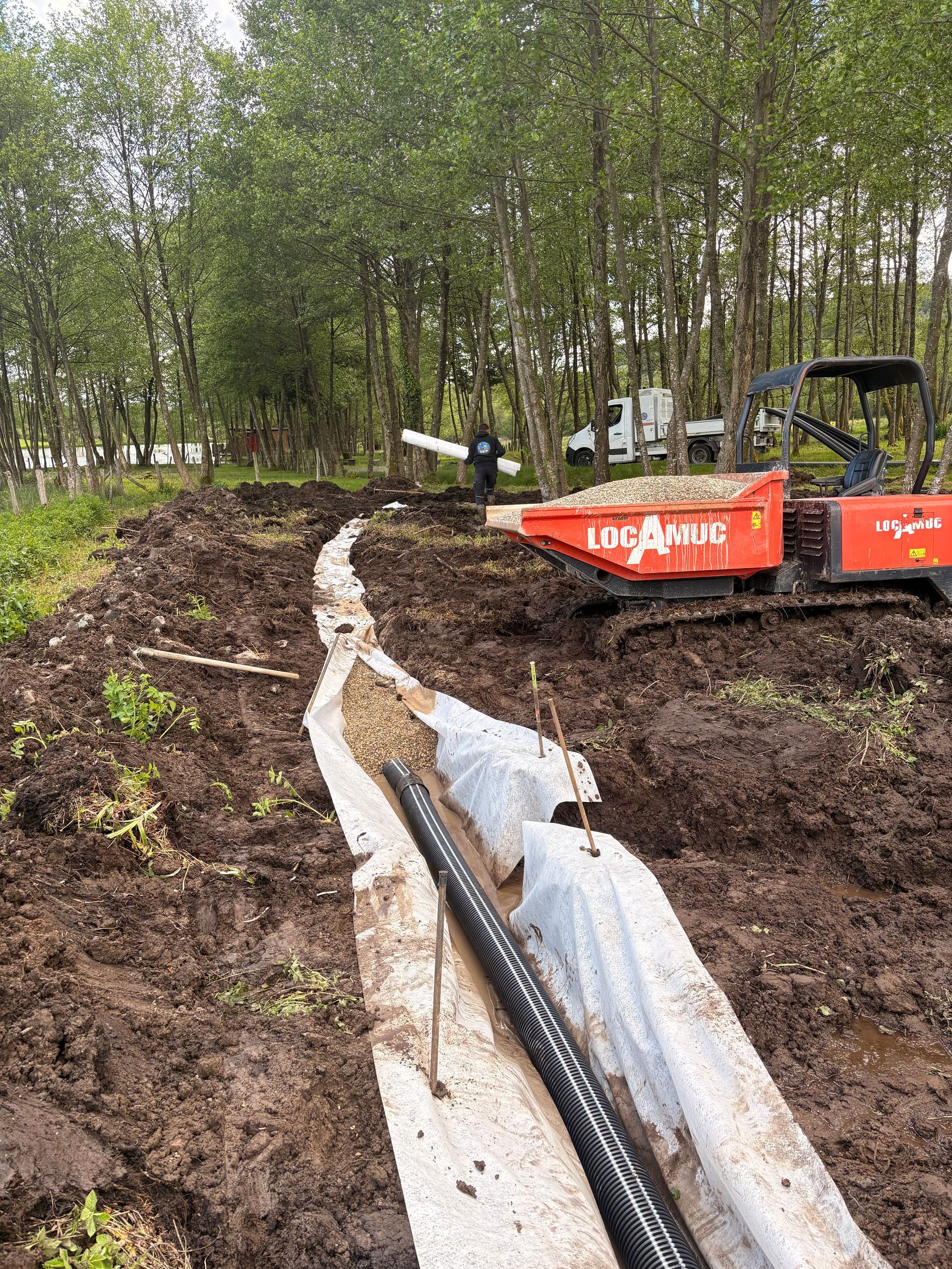 Tranchée de chantier avec un gros tuyau noir à côté d'une excavatrice jaune et une maison en arrière-plan
