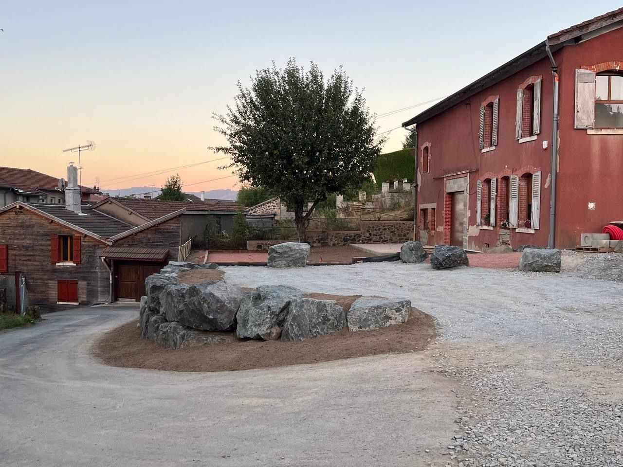 Cour de village paisible avec puits en pierre, arbre et maisons en briques rouges au coucher du soleil