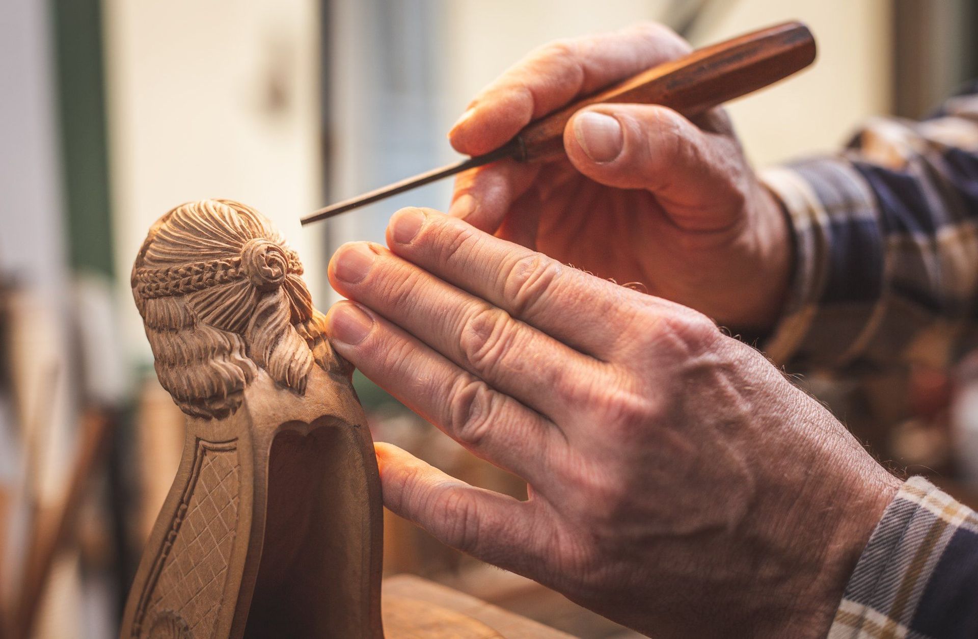 Hände schnitzen mit einem kleinen Werkzeug eine Holzfigur,