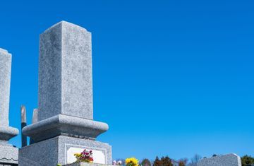 Grauer Grabstein vor einem klaren blauen Himmel. Blumen davor.
