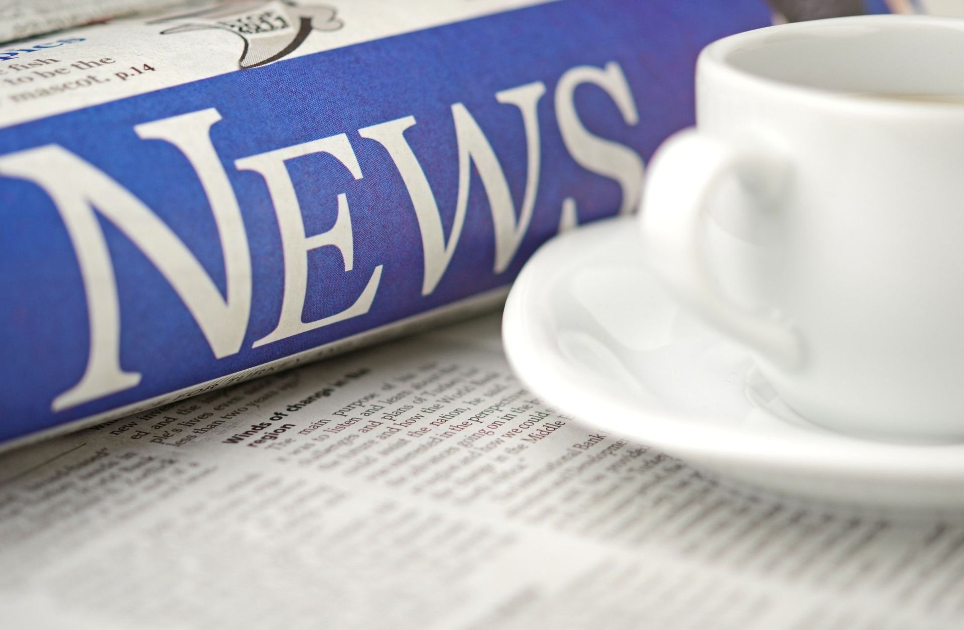Blaue Zeitung mit weißem „NEWS“ und weißer Kaffeetasse auf Untertasse.
