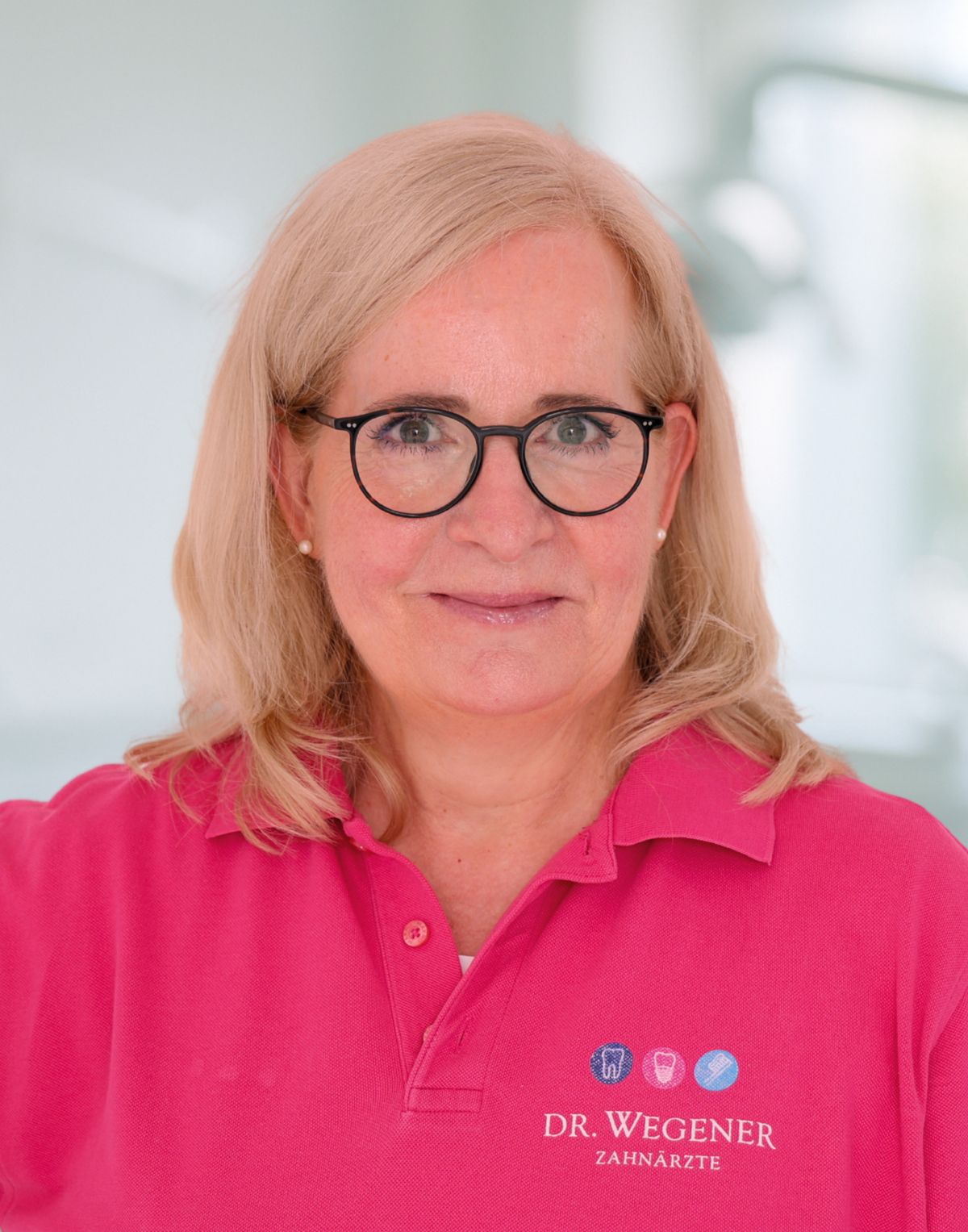 Porträt einer lächelnden Person mit Brille, die ein rosa Poloshirt trägt